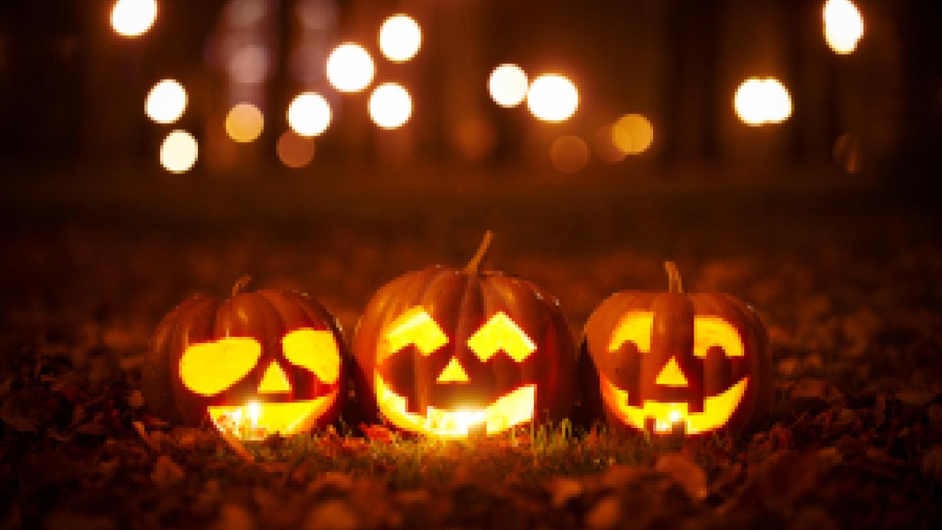 three jack-o-lanterns sitting on leaves in a park at night