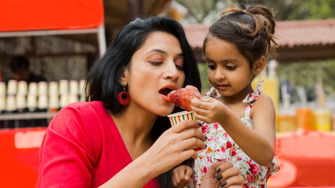 Mother and daughter at a multicultural festival enjoying a delicacy from one of the food vendors