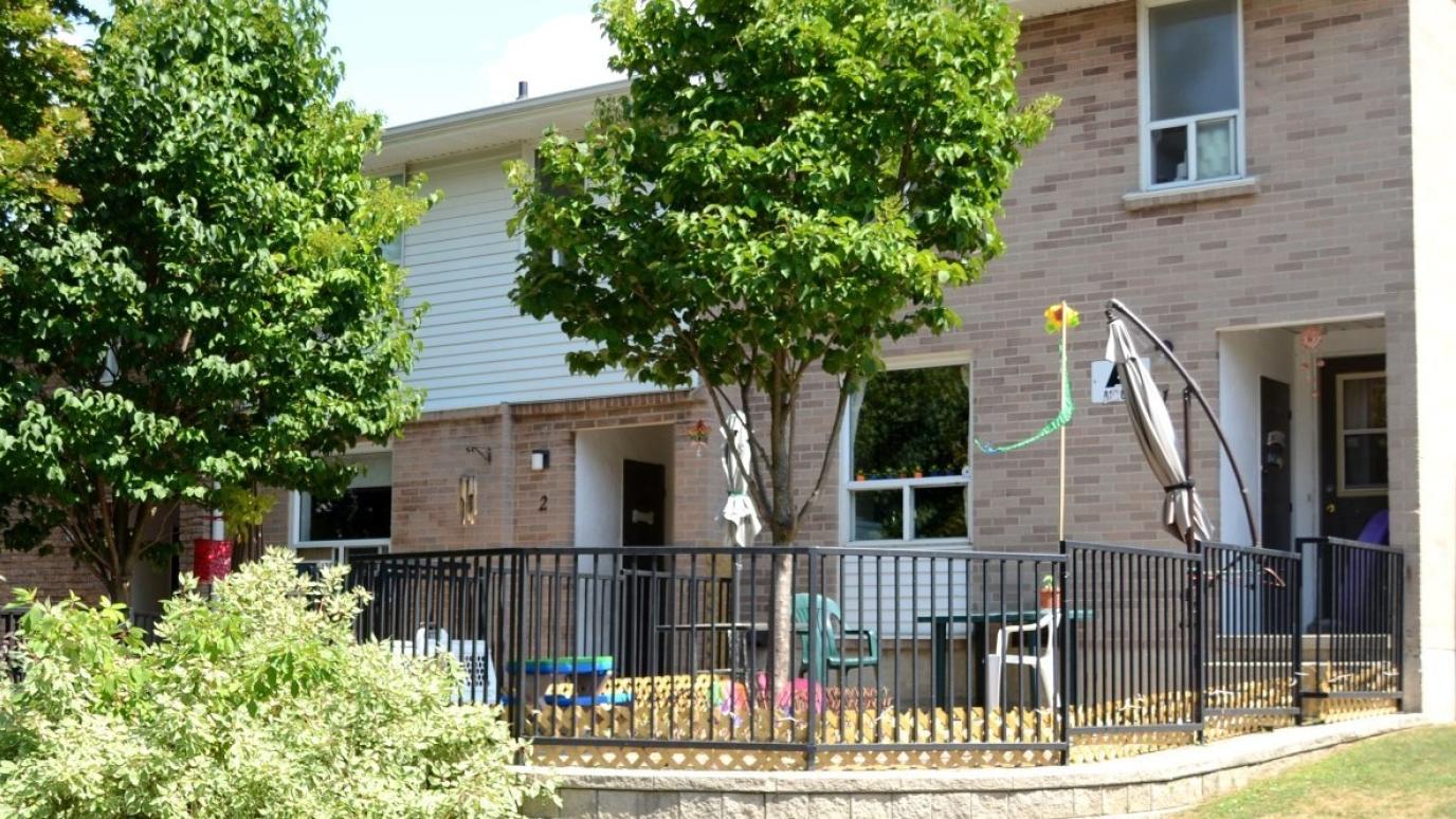 Exterior of 12 Sunset Road, Guelph. It is a row of townhouses with trees and fenced yards in front.