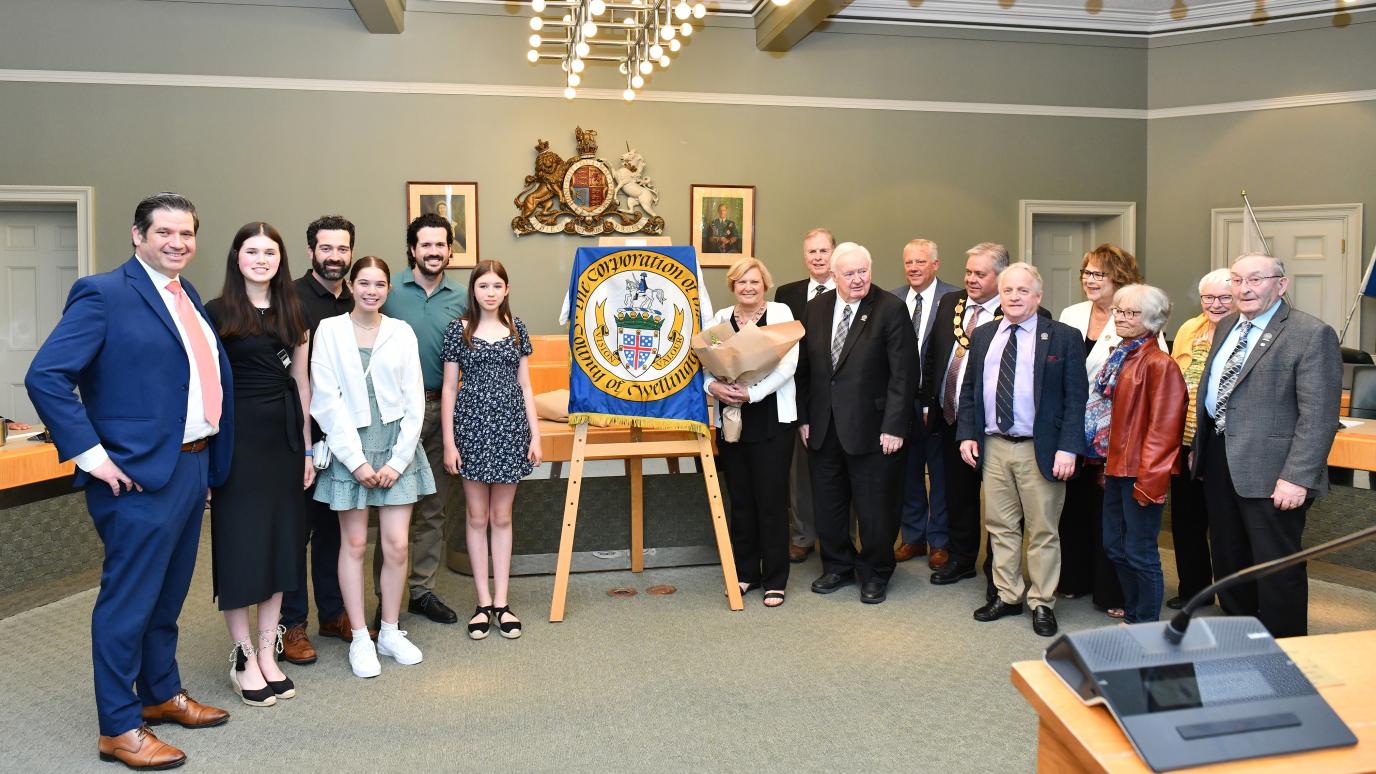 A group of people stand on either side of a frame covered with a County of Wellington flag.