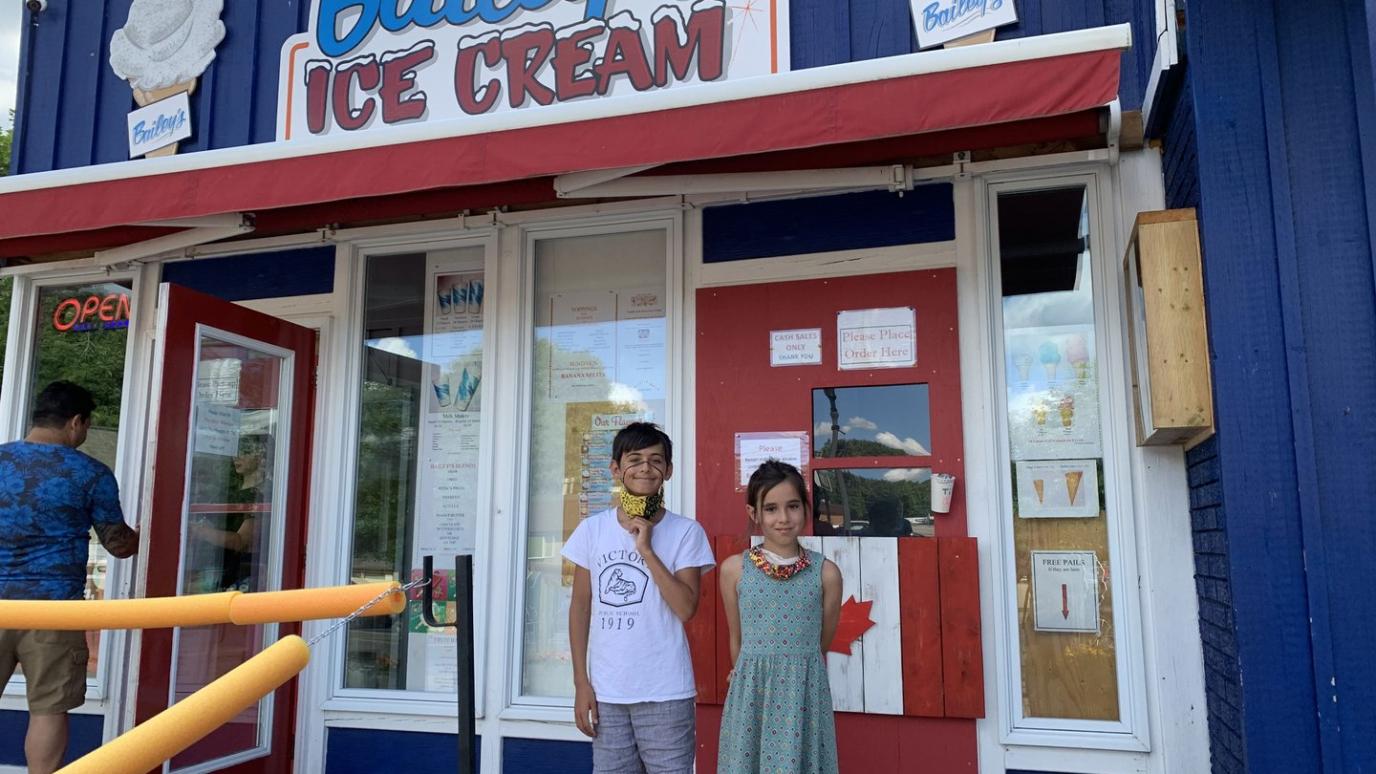 A young boy and girl smile while standing in front of the "Bailey's Ice Cream" storefront.
