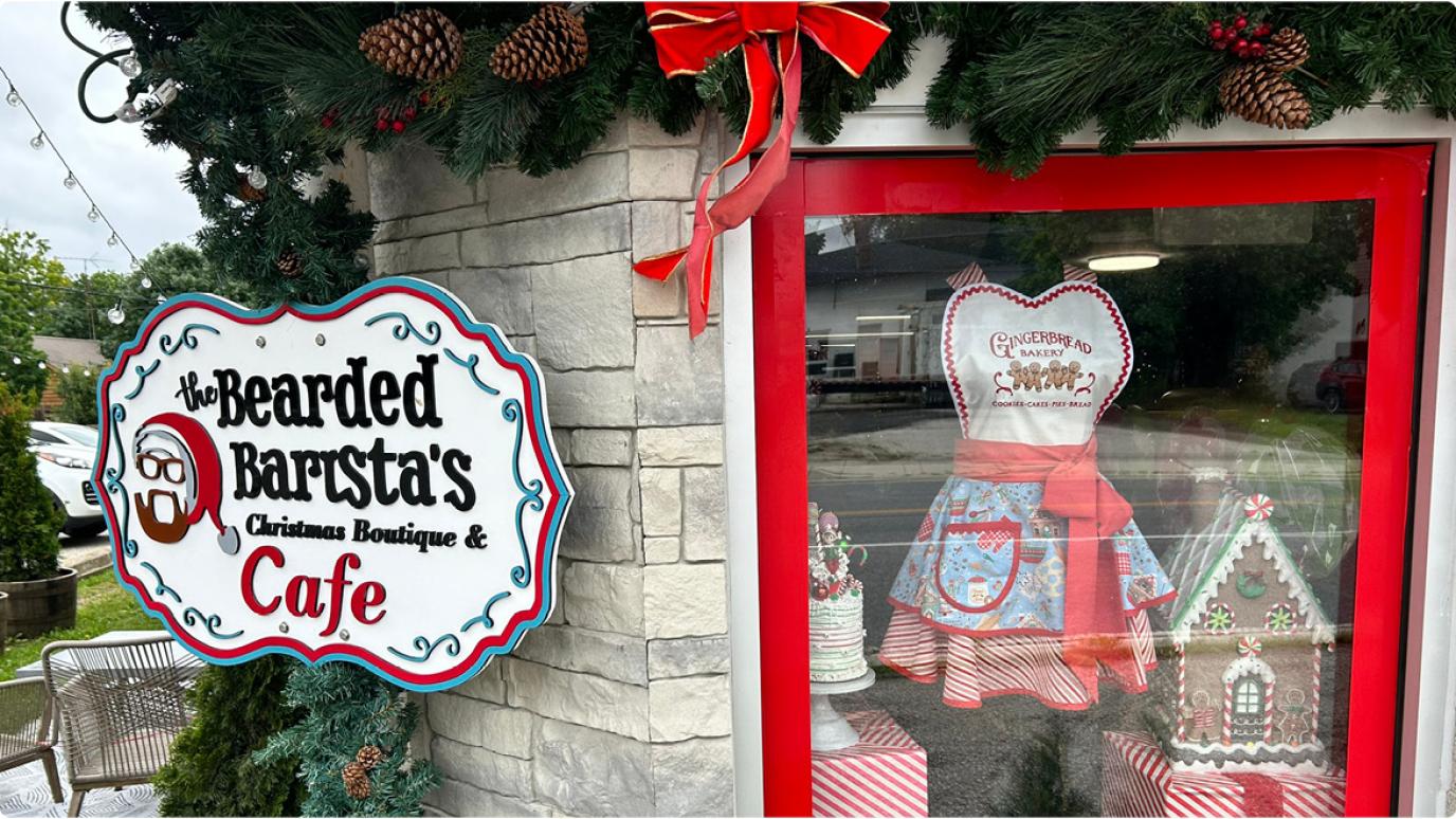 Image of Christmas decor in the storefront window next to a sign of The Bearded Barista's Christmas Boutique and Cafe. 