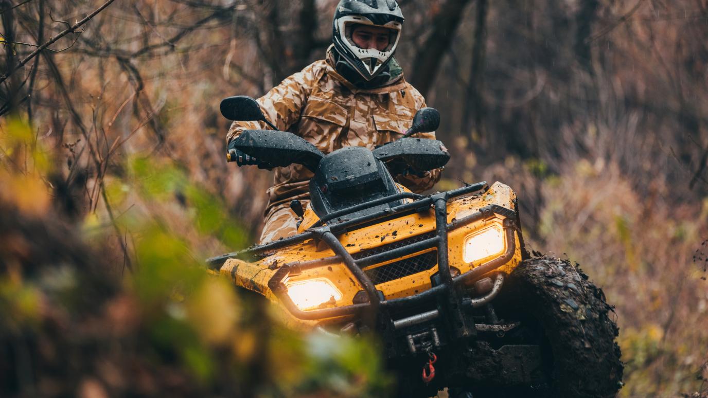 A person in camo drives on an ATV through a forest. 