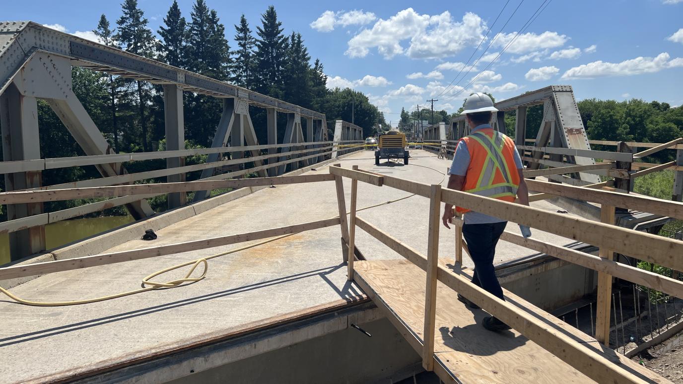 A man in construction attire walks over a wood platform to get to the old simmons bridge