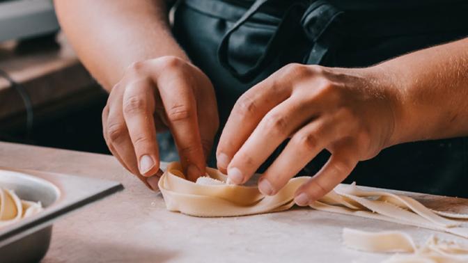 Chef woman's hands making tagliatelle pasta