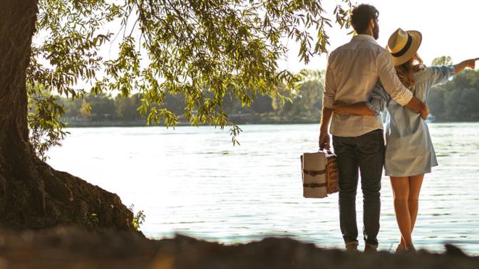 Couple standing by a lake with a picnic basket enjoying the summers day
