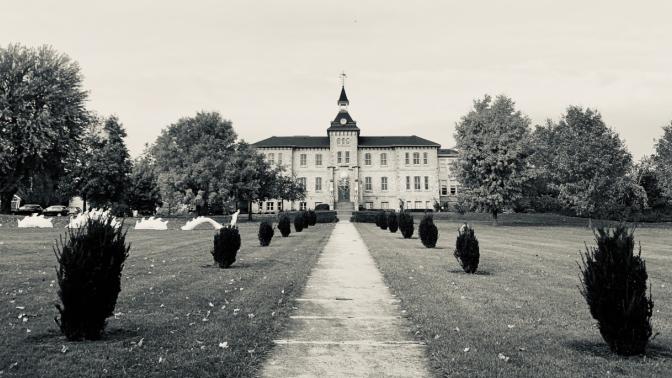 A sepia-toned photo of the Wellington County Museum and Archives, taken at a distance to show the front lawn, trees, and front of the Museum.