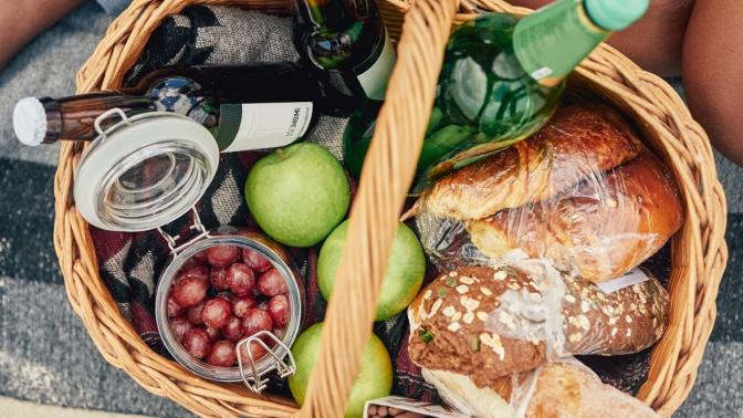 gift basket full of fruit, bread and beverages on a blanket.