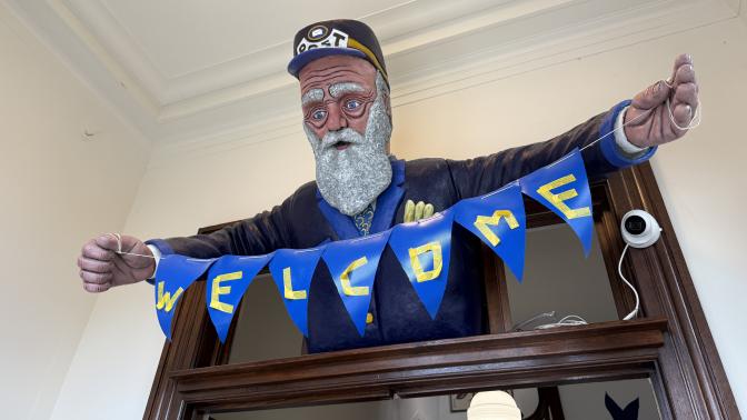 postman statue above doorway holding a blue "WELCOME" banner