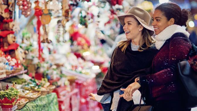 Two women looking at holiday items while carrying bags