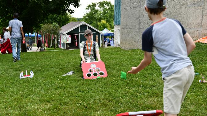 Two young boys play a beanbag toss game on a grassy field during the Multicultural Festival.