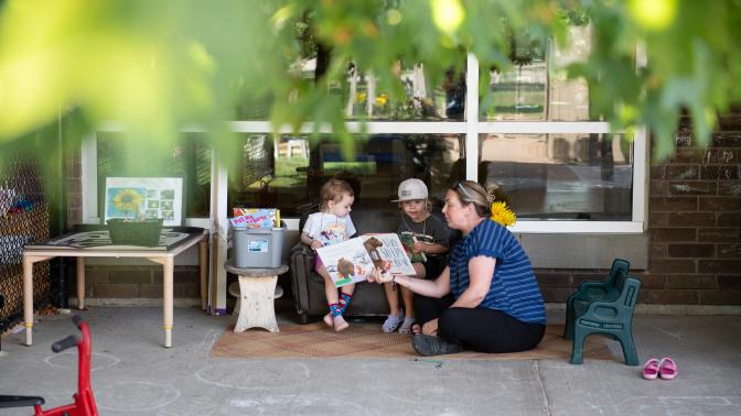 An ECE is reading a book to two kids sitting beside her. 