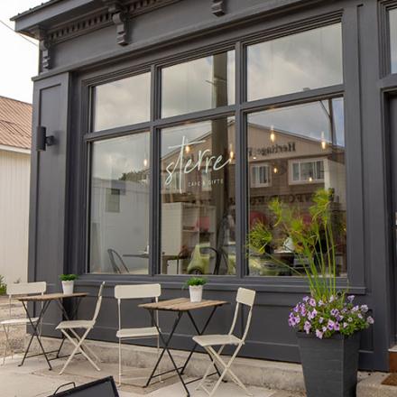 The modern interior of a gift shop and cafe with large front windows and a table and chairs out front. 
