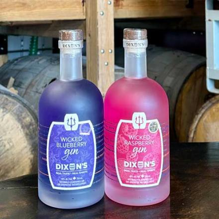 A colourful purple and pink gin bottles sit on a table with casks of gin in the backgroun