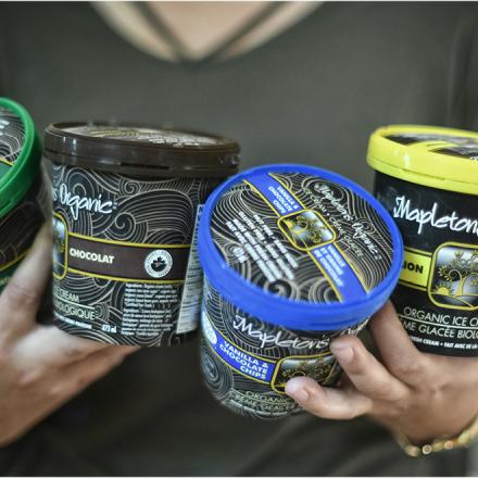 A woman holds four pints of Mapleton's ice cream in her hands, all with different colour tops. 