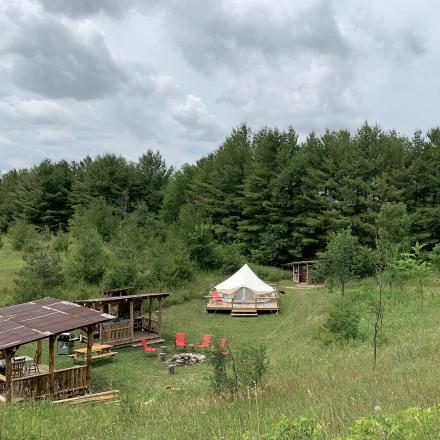 glamping tent in field with firepit and chairs