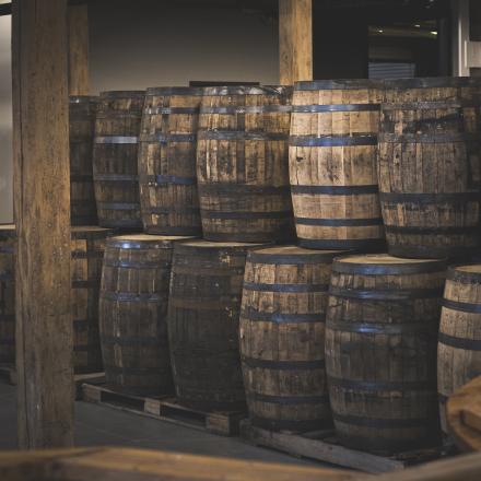 A dim image shows rows of wooden barrels stacked in a cellar.