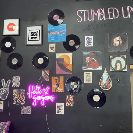 Black wall with records, posters and a neon sign on it