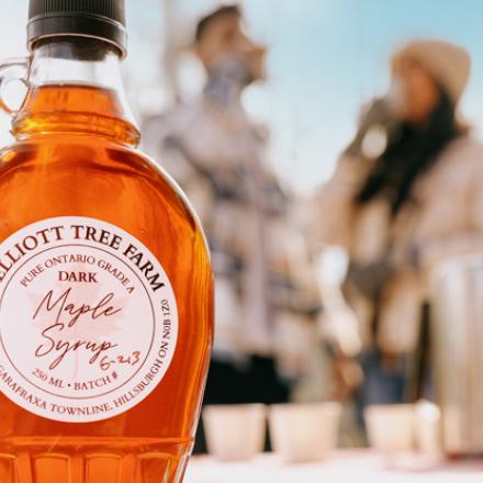 close up of two bottles of maple syrup with people blurred in the background