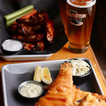 fish and chips with coleslaw and lemon and a plate of barbecue wings with a dipping sauce with a glass of beer