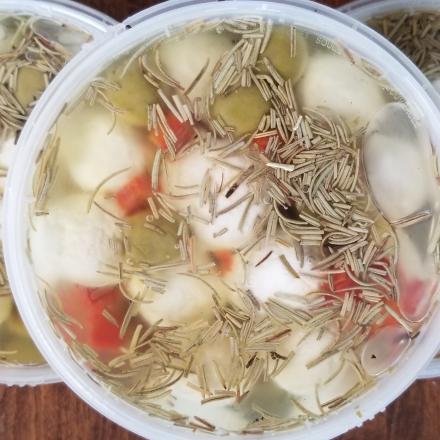 three plastic containers filled with marinated chèvre (goat cheese) balls submerged in oil, topped with dried herbs like rosemary and bits of red pepper