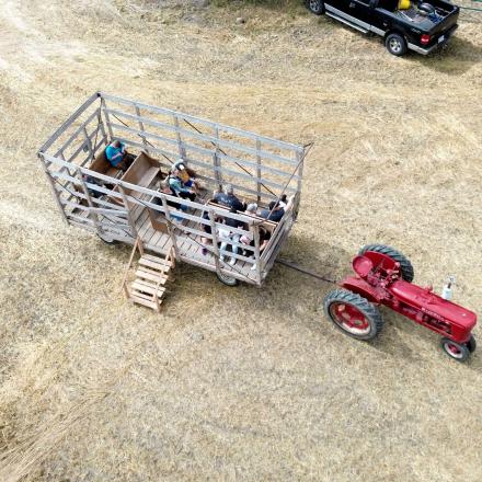 High-angle view of a vintage red tractor pulling a large metal hay wagon filled with people