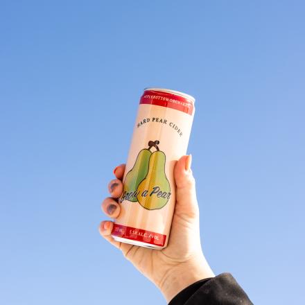 A hand holding up a can of pear cider against a clear blue sky.