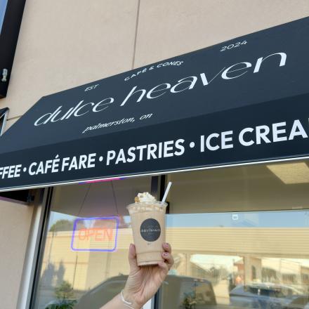 hand holding ice beverage in front of a black business sign