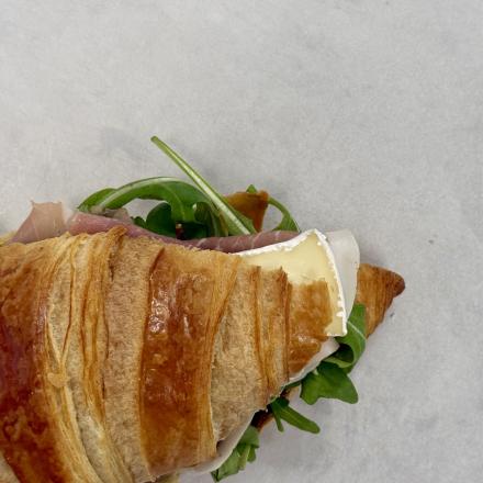 top view of a flaky croissant with brie, prosciutto and arugula