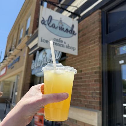 hand holding flavoured lemonade in front of store sign