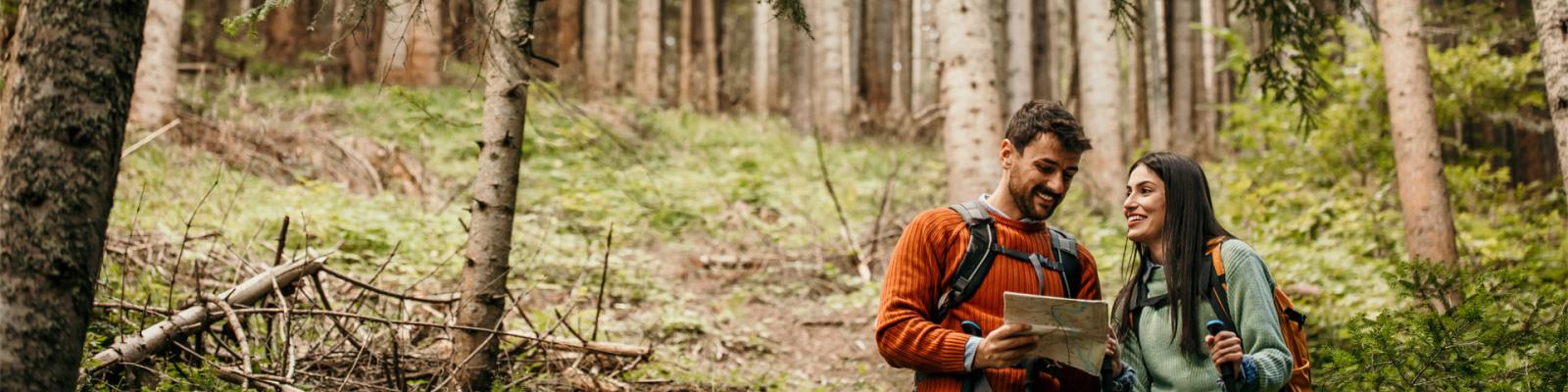 Young man and woman backpacking couple stop to look at a map along a forest trail
