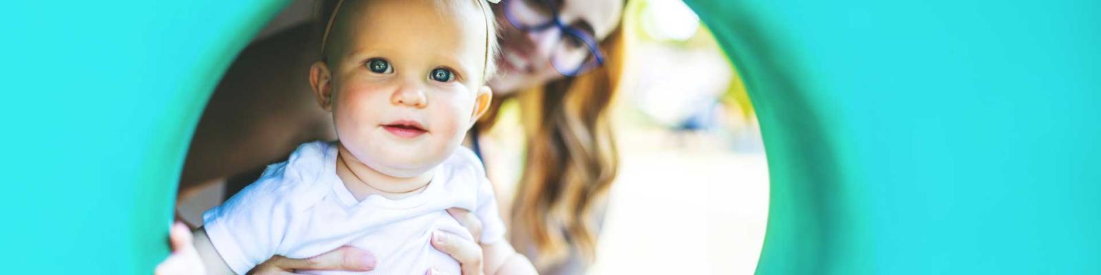 Childcare provider and infant baby play together in a play structure outdoors