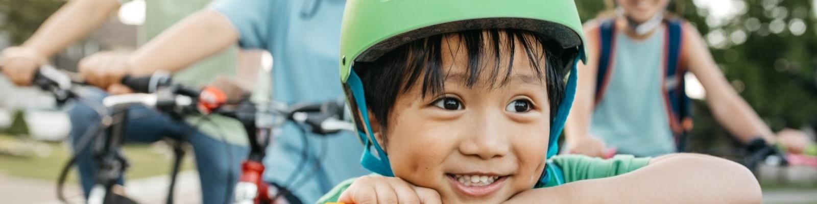 Young boy leaning over the handlebars of his scouter with a broad smile and family standing in the background.