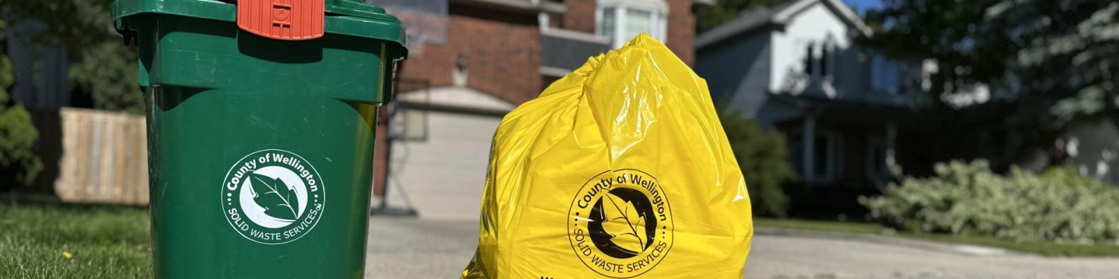 a green bin for organic waste and a yellow Wellington County user pay garbage bag sit at the end of a driveway in an urban neighbourhood