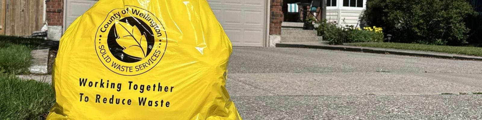 a yellow Wellington County user pay garbage bag sits at the end of a driveway