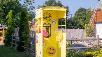 An art installation featuring a bright yellow telephone booth covered in smiley faces sits downtown Clifford