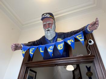 postman statue above doorway holding a blue "WELCOME" banner