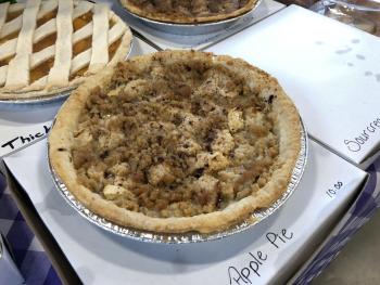 close-up shot of a crumb-topped apple pie in a silver tin, resting on a white box labeled Apple Pie