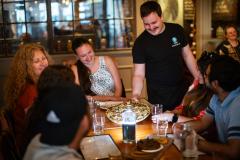 people sitting around table smiling while being served pizza