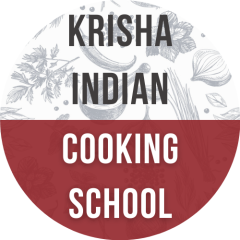 A round logo. The top half is white, with illustrated grey cooking ingredients in the background. The bottom half is red. The text of the logo reads "Krisha Indian Cooking School".