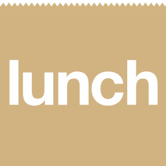 A logo for Lunch Inc. in the shape of a brown paper lunch bag. On the bag is the word "Lunch" in white font.