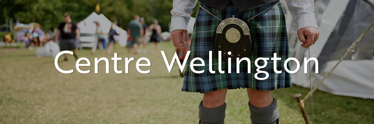 A man wearing a tartan kilt, sporran, and kilt hose in a park.