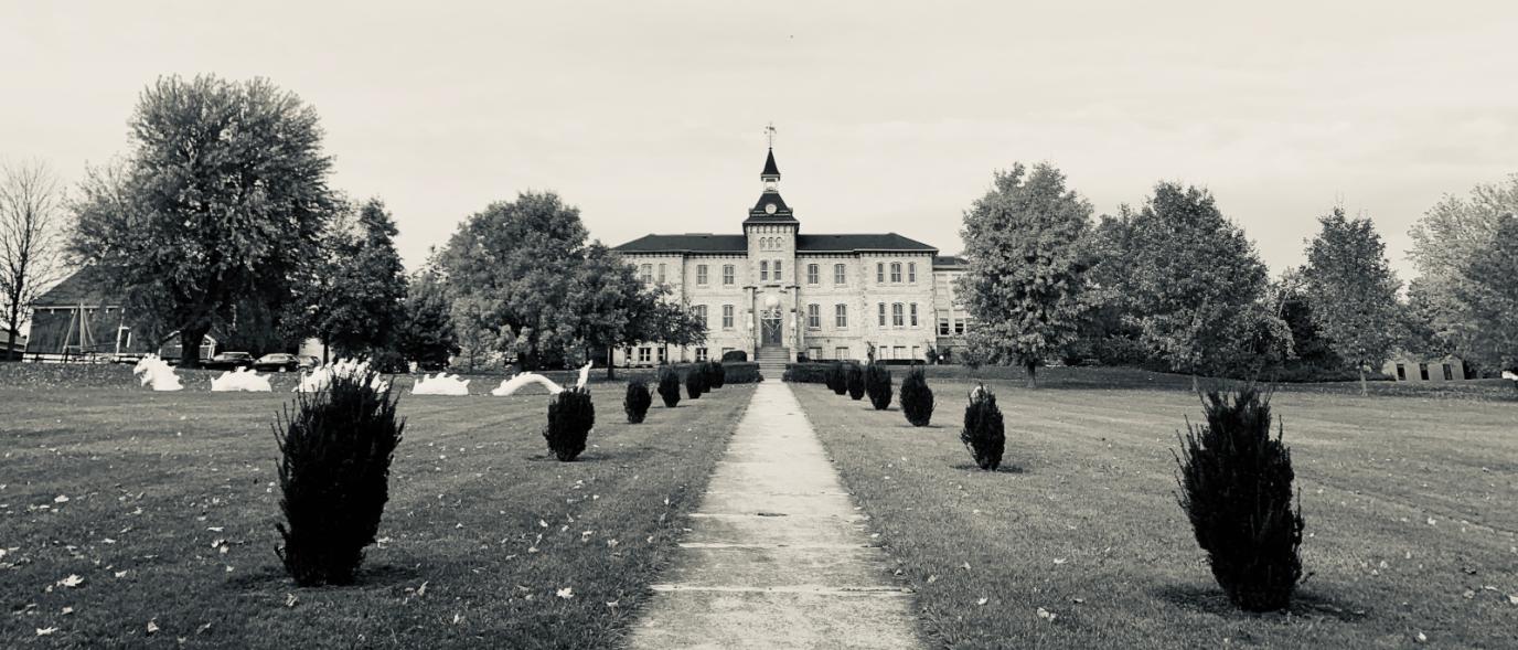 A sepia-toned photo of the Wellington County Museum and Archives, taken at a distance to show the front lawn, trees, and front of the Museum.