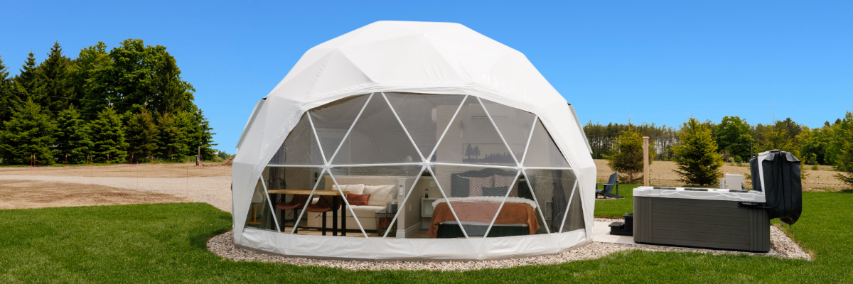 A white glamping geodesic dome with a large window section and an outdoor hot tub.