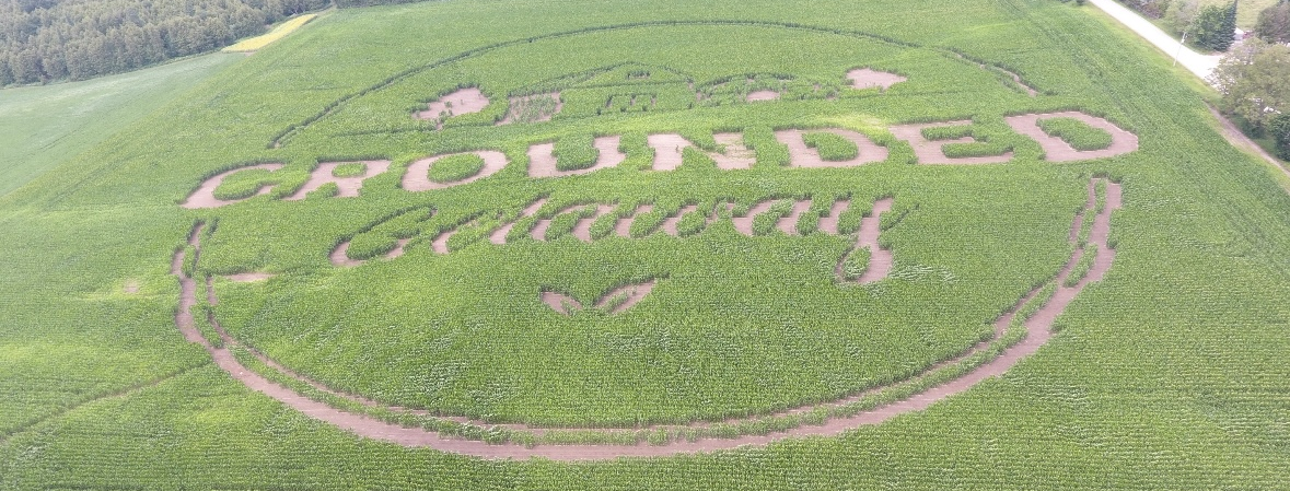 Aerial view of a corn maze featuring the text "GROUNDED Getaway" inside a circular design carved into a green field.